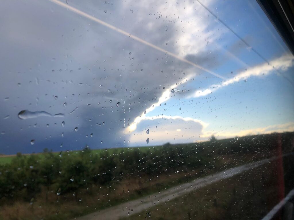 A photograph I took from the train showing rain clouds and blue skies on the horizon of a landscape.